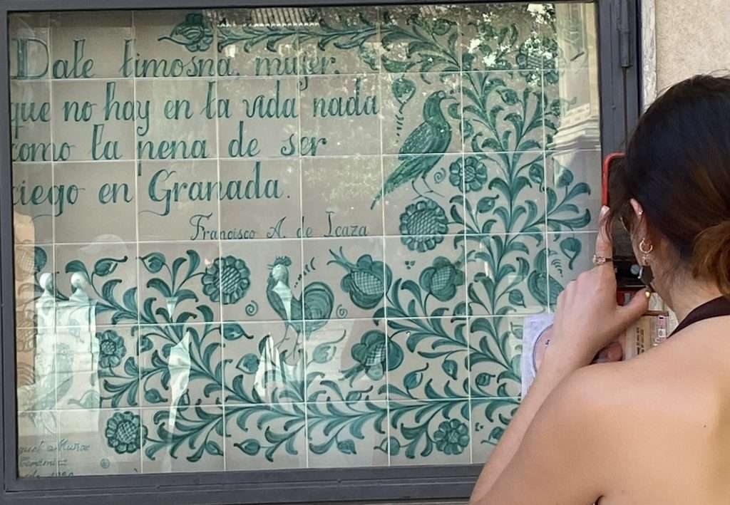 Mujer haciendo una foto de un azulejo con un poema granadino.