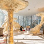 Habitación decorada con esculturas cubiertas con lana, con cojines en el suelo y chica sentada escuchando música