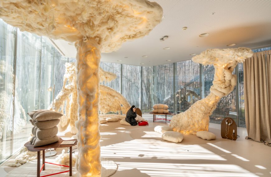 Habitación decorada con esculturas cubiertas con lana, con cojines en el suelo y chica sentada escuchando música