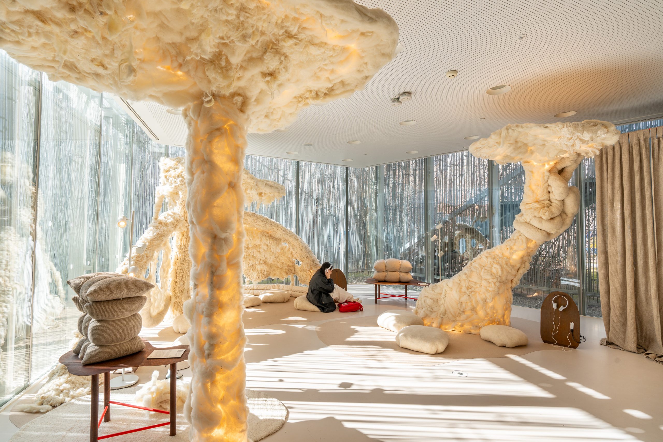 Habitación decorada con esculturas cubiertas con lana, con cojines en el suelo y chica sentada escuchando música