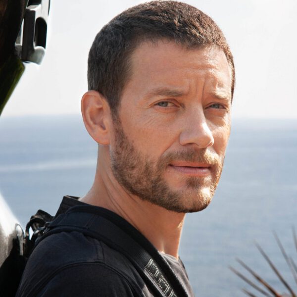 Músico Matthieu Saglio con el violonchelo en la espalda, con el cielo y el mar al fondo. Foto Ana Guimaras