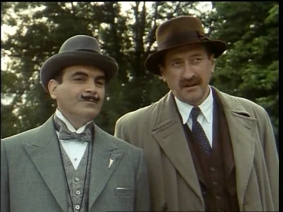 Actores en el parque al fondo árboles en escena de la serie Poirot. Vestidos con trajes pajarita, corbata y sombreros